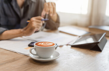 Latte glass in the background of a close-up photo of a business man working with a tablet and graph data.