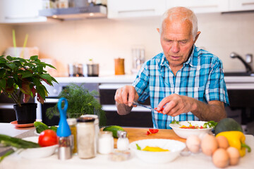Obraz na płótnie Canvas senor man preparing fresh vegetable salad at home in the kitchen