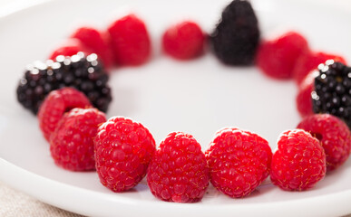 raspberries and blackberries laid out on a white plate in circle