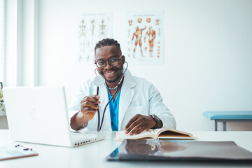 Fototapeta premium Doctor in office working on laptop. Male doctor working at office desk and smiling at camera, office interior on background. 