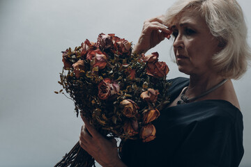 Upset elderly woman hold withered dry old rose flowers bouquet