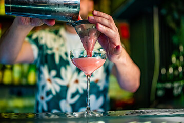 man hand bartender pouring pink sweet and sour refreshing cocktail in glass on the bar counter