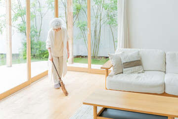 箒で部屋を掃除するシニア女性 © polkadot