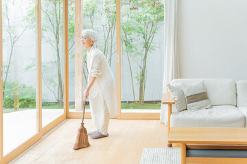 箒で部屋を掃除するシニア女性