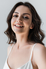 Portrait of smiling woman with makeup looking at camera isolated on grey.