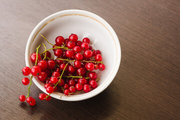 Sprigs of red currant in a white bowl closeup top view. Sweet red currant spilling out from the bowl. Currant organic berries harvest - healthy eating and food concept