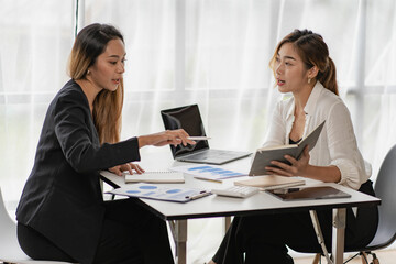Fototapeta premium Two Asian business women working on a financial graph and a laptop. in the presentation and review of the business plan Joint financial marketing strategies in the meeting room with new employees in t