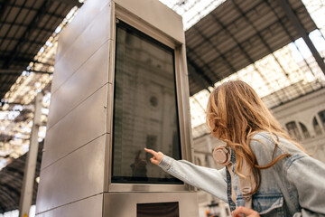 Pleasant young caucasian woman buys train ticket from vending machine at station. Blonde wears casual clothes in spring. Leisure lifestyle concept
