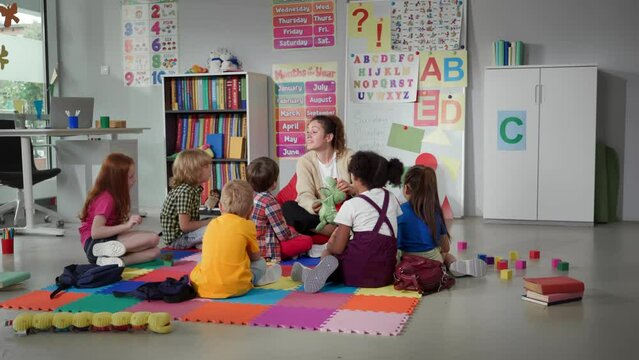 children sitting on floor while caring teacher explains lesson using toy in kindergarten