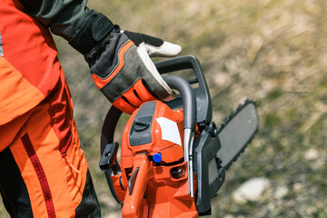 Close up view of an hand holding a chainsaw. Lumberjack at work wears orange personal protective...
