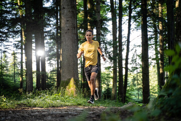 Junger dunkelh&auml;utiger Mann in Sportkleidung l&auml;uft im Wald beim Trailrunning
