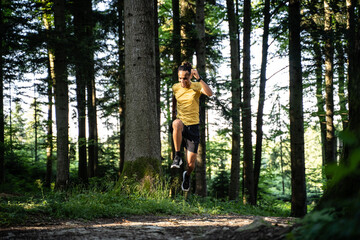 Junger dunkelh&auml;utiger Mann in Sportkleidung spring w&auml;hrend dem Laufen im Wald beim Trailrunning