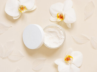 Fototapeta na wymiar Opened Cream jar with a blank lid near orchid flowers on light beige top view. Cosmetic Mockup