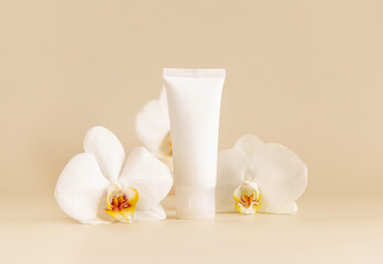 Fototapeta na wymiar White cream tube near white orchid flowers on light beige close up. Mockup. Skincare product