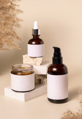 Cosmetic bottles on beige stones near dry pampas grass on light beige close up. Labels Mockup