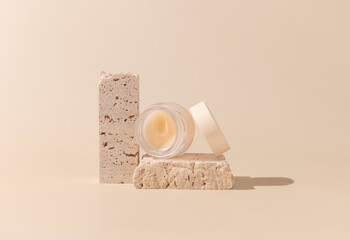 Glass Cosmetic jar on travertine stones on light beige close up. Skincare beauty product
