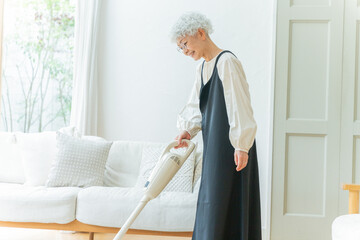 部屋でハンディ掃除機をかけるシニア女性 © polkadot