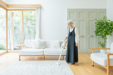 部屋でハンディ掃除機をかけるシニア女性 © polkadot