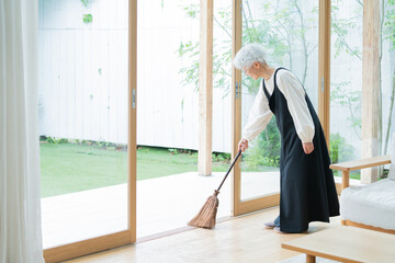 箒で部屋を掃除するシニア女性