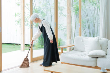 箒で部屋を掃除するシニア女性 © polkadot