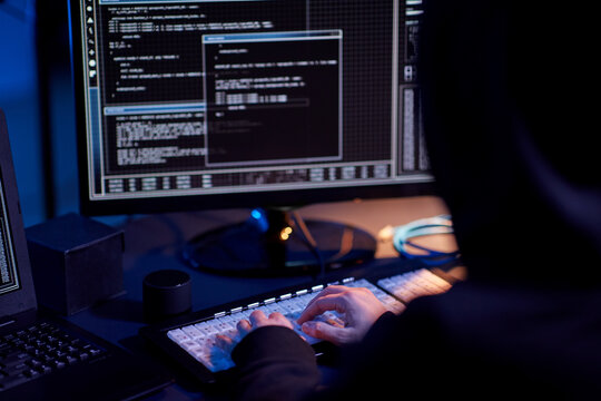 cybercrime, hacking and technology concept - close up of hacker in dark room writing code or using computer virus program for cyber attack