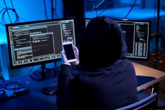 cybercrime, hacking and technology concept - hacker with smartphone using computer virus program for cyber attack in dark room