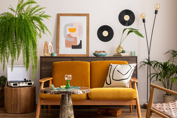 Vintage retro composition of living room interior with mock up poster frame, yellow velur sofa, plants, wooden commode, coffee table and personal accessories. Stylish home decor. Template. 