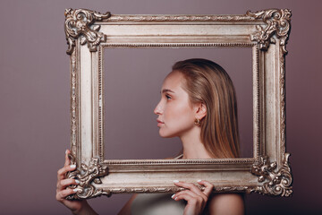 Millenial young woman blonde hair holds gilded picture frame in hands face portrait.