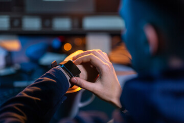 cybercrime, hacking and technology concept - close up of male hacker in dark room with smart watch and computer carries out cyber attack in dark room