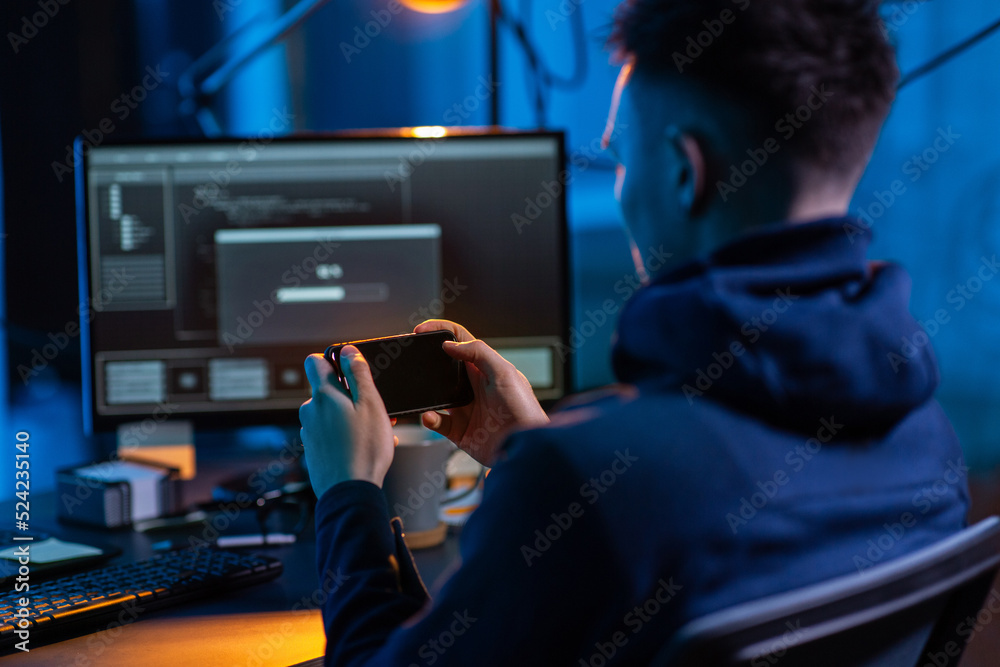 Poster cybercrime, hacking and technology concept - close up of male hacker with smartphone using computer 