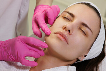 Close up face of thread lifting procedure. Professional cosmetologist in pink medical gloves...