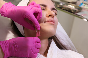 Close up face of thread lifting procedure. Professional cosmetologist in pink medical gloves inserting needles in chin scin. Anti-aging treatment and face lift in cosmetology clinic. Pretty woman fac