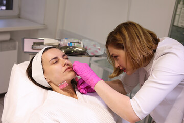 Thread lifting procedure. Professional cosmetologist in pink medical gloves inserting needles in chin scin. Anti-aging treatment and face lift in cosmetology clinic Close up face of pretty woman. 