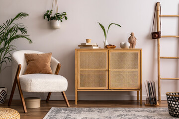 Stylish composition of scandi living room interior with white armchair, rattan commode, design furniture, decoration, carpet, plant and personal accessories. Beige wall. Template.	
