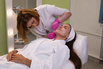 Obraz na płótnie Canvas Thread lifting procedure. Professional cosmetologist in pink medical gloves inserting needles in chin scin. Anti-aging treatment and face lift in cosmetology clinic Close up face of pretty woman. 