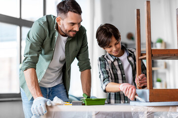 renovation, diy and home improvement concept - happy smiling father and son in gloves with paint brush painting old wooden table in grey color