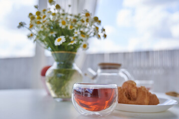 Transparent glass Cup of tea in nature. The concept of breakfast in the backyard of the house. Early morning, tea and kettle. In the cup you can see the reflection of the sky and a one-story house.