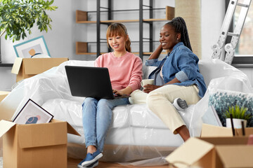 moving, people and real estate concept - happy smiling women with laptop computer and boxes at new home