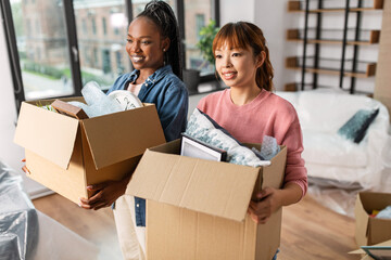 moving, people and real estate concept - happy smiling women with boxes at new home
