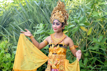 Pretty girl in traditional Balinese yellow costume with make-up in palm forest.