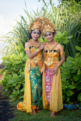 Fototapeta na wymiar Pretty girls in traditional Balinese yellow costume with make-up in palm forest.