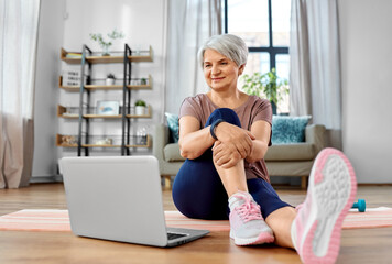 sport, fitness and healthy lifestyle concept - smiling senior woman exercising with laptop computer on mat at home