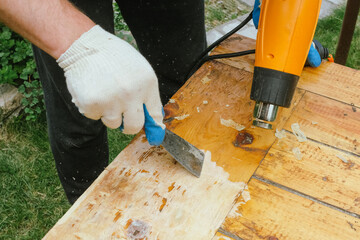 Man removing old varnish and paint from wood using scraper and heat gun. Restoration work of old...