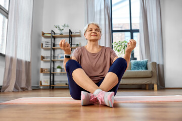 sport, fitness and healthy lifestyle concept - happy senior woman meditating on exercise mat at home