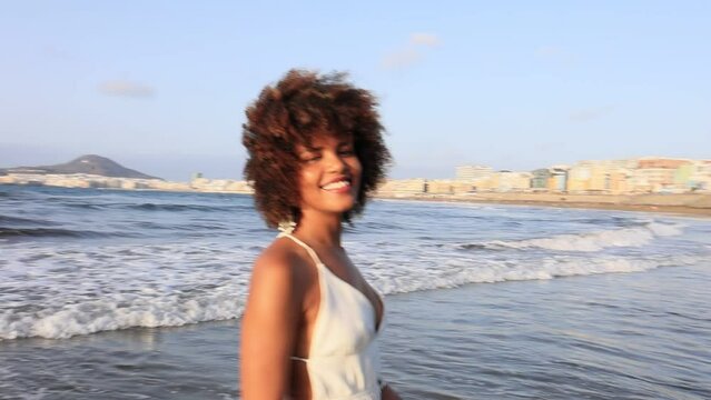 Beautiful young African girl in white dress walking happily along the beach