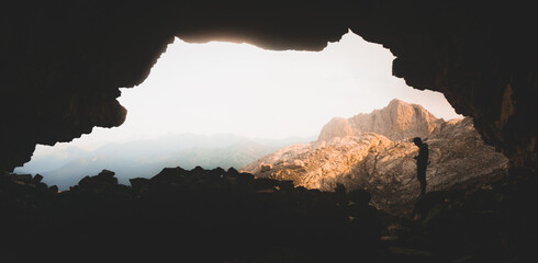 Sunrise inside a cave looking outside with a man standed up and with his phone