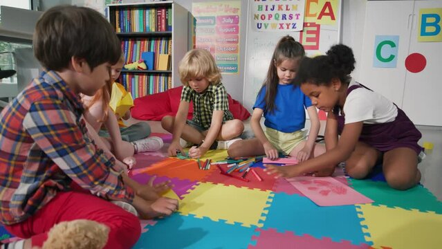 group of preschool children draw in classroom sitting on floor