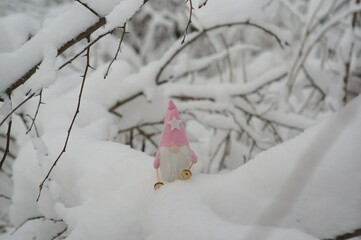 A toy gnome on skis in the winter forest. Christmas figurines.