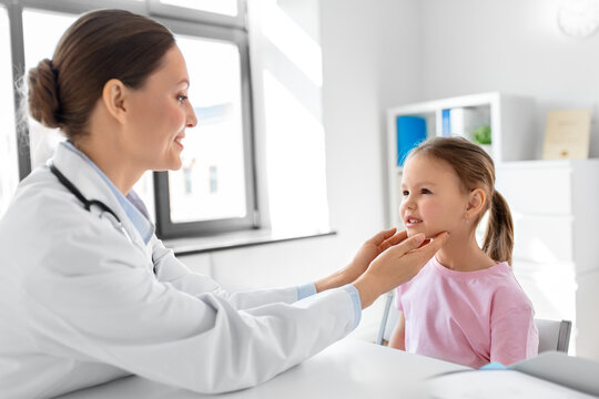 medicine, healthcare and pediatry concept - female doctor or pediatrician checking little girl patient's tonsils on medical exam at clinic