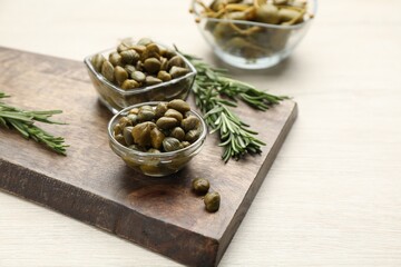 Delicious pickled capers and rosemary twigs on white wooden table, space for text